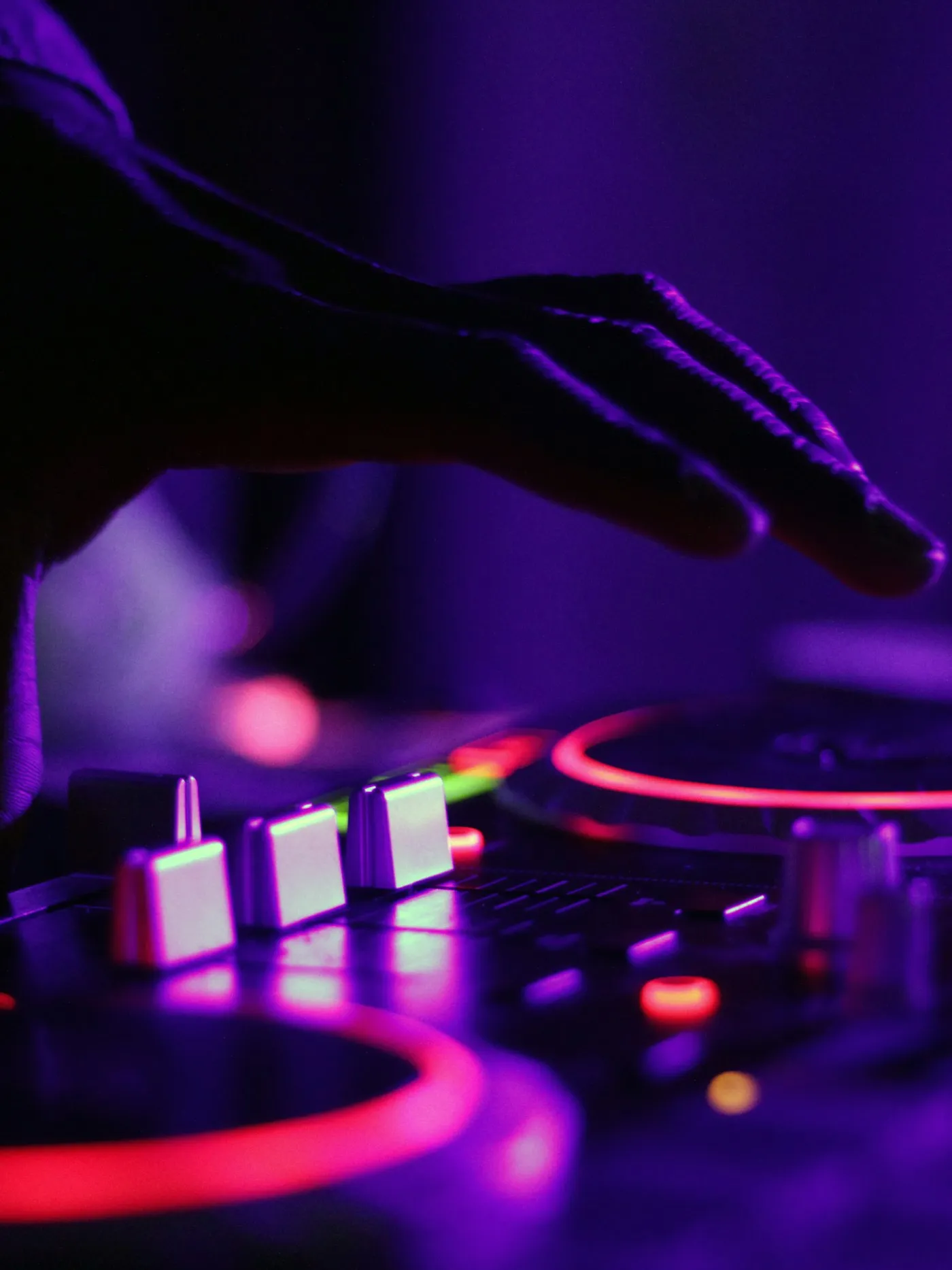 Main d'un DJ sur une platine et une table de mixage, éclairées de violet et de rouge